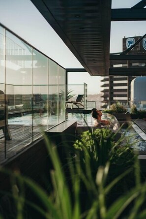 Zona de piscina moderna al aire libre con paredes de vidrio, sillas de descanso y plantas en macetas.