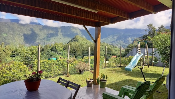 A covered patio with a table and chairs, a slide, and a view of mountains.