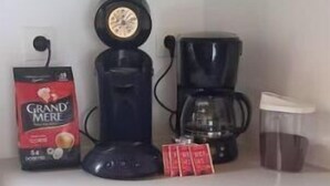 A kitchen with a coffee maker, a coffee pot, a bag of coffee, and a container of coffee grounds.
