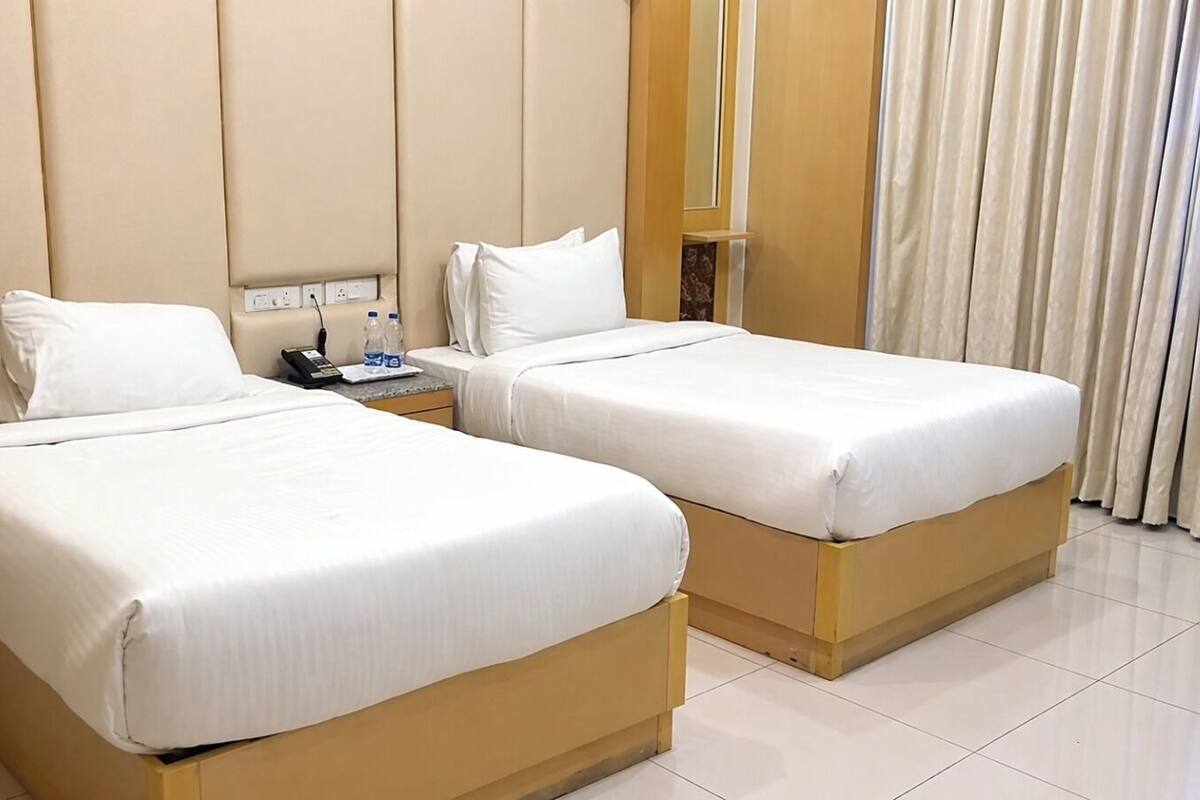 Twee eenpersoonsbedden met witte lakens in een hotelkamer.
