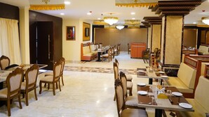 A hotel dining area with multiple tables and chairs, chandeliers, and a reception desk. - AR Thanga Kottai (Tirupattur)