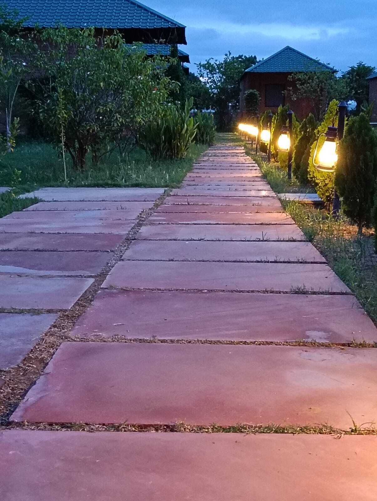 A paved pathway leading to a building with a tiled roof, surrounded by greenery and illuminated by outdoor lights.