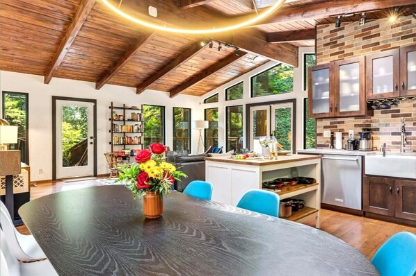 A spacious dining area with a large wooden table, blue chairs, and a vase of red flowers.