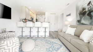 A modern living room with a beige sofa, patterned ottoman, and a blue rug. - The Shores Lake View Condo Unit 5574 (Williamsburg)