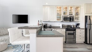 A modern kitchen with a flat-screen TV, stainless steel appliances, and a seating area with a patterned rug. - The Shores Lake View Condo Unit 5574 (Williamsburg)
