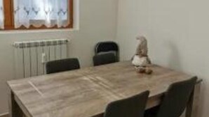 Zona pranzo con tavolo in legno, quattro sedie, un termosifone e una finestra con tenda.