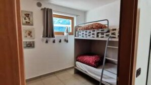 Una stanza piccola e funzionale con un letto a castello, una finestra con tende e alcuni elementi fissati alla parete.