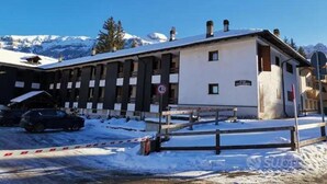 Un edificio con tetto imbiancato dalla neve, un cartello che indica una valutazione di 4.5 stelle e sullo sfondo montagne innevate.