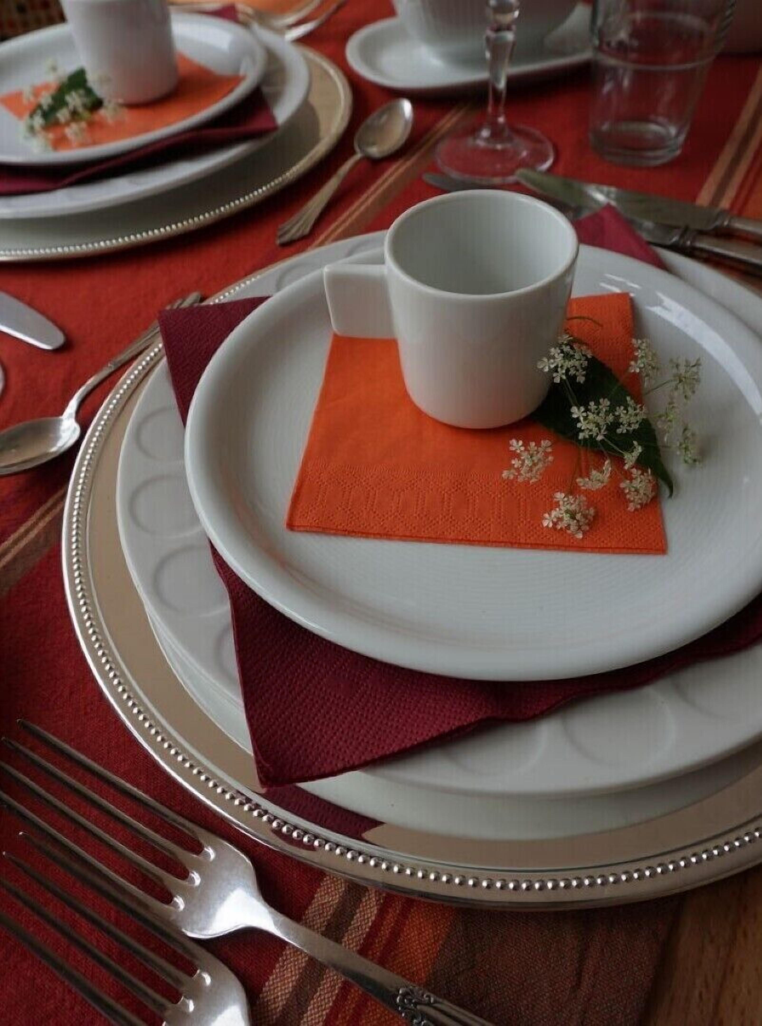 A table set with white plates, silverware, and a white cup on a red napkin.