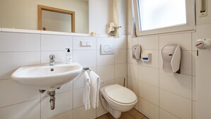 Un baño con lavabo, inodoro, secador de manos y dispensador de jabón.