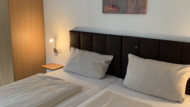 Habitación de hotel con dos camas, un armario de madera, una mesita de noche y un cuadro colgado en la pared.