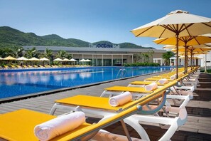 Ett område vid poolen med solstolar och parasoller, en klarblå pool och en byggnad i bakgrunden med skylten ”The Ocean Hall”.