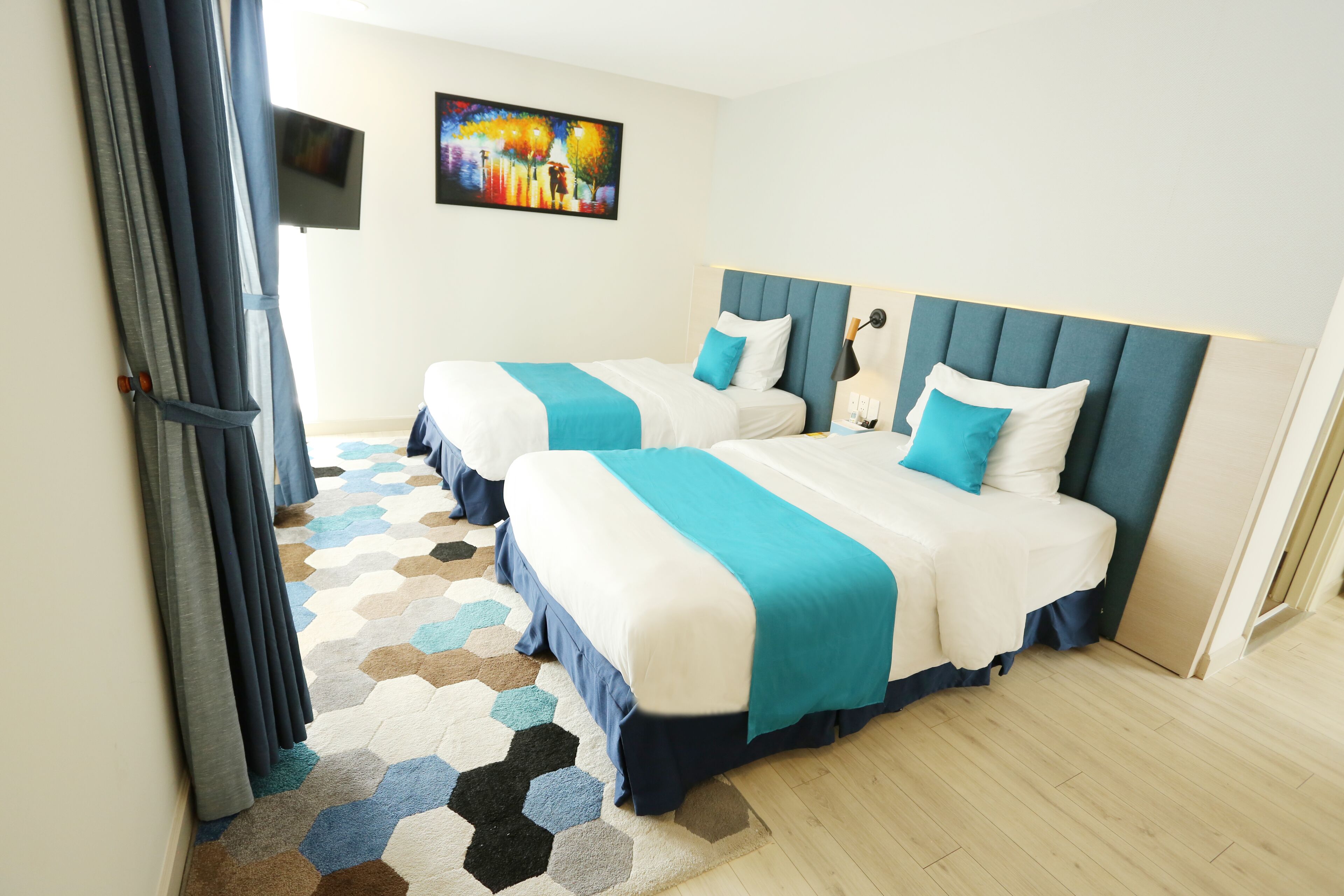 A hotel room with two beds, a colorful hexagonal rug, and a painting on the wall.