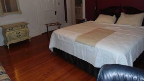 A bedroom with a large bed, a dresser, a mirror, and a door leading to another room. - Peace Apartment, upstairs with king size bed. (Anniston)