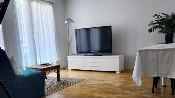 Ein Wohnzimmer mit Fernseher auf einem weißen Schrank, einem blauen Sofa, einem kleinen Tisch und einer Pflanze.
