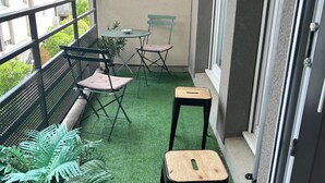 Ein Balkon mit Kunstgrasanlage, zwei Klappstühlen, einem kleinen Tisch und einem Blumentopf.