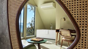 A room with a large mirror reflecting a modern interior, including a white bathtub, a desk with a chair, and a chessboard on a table. - Treat Aranya Resort (Kumbhalgarh)