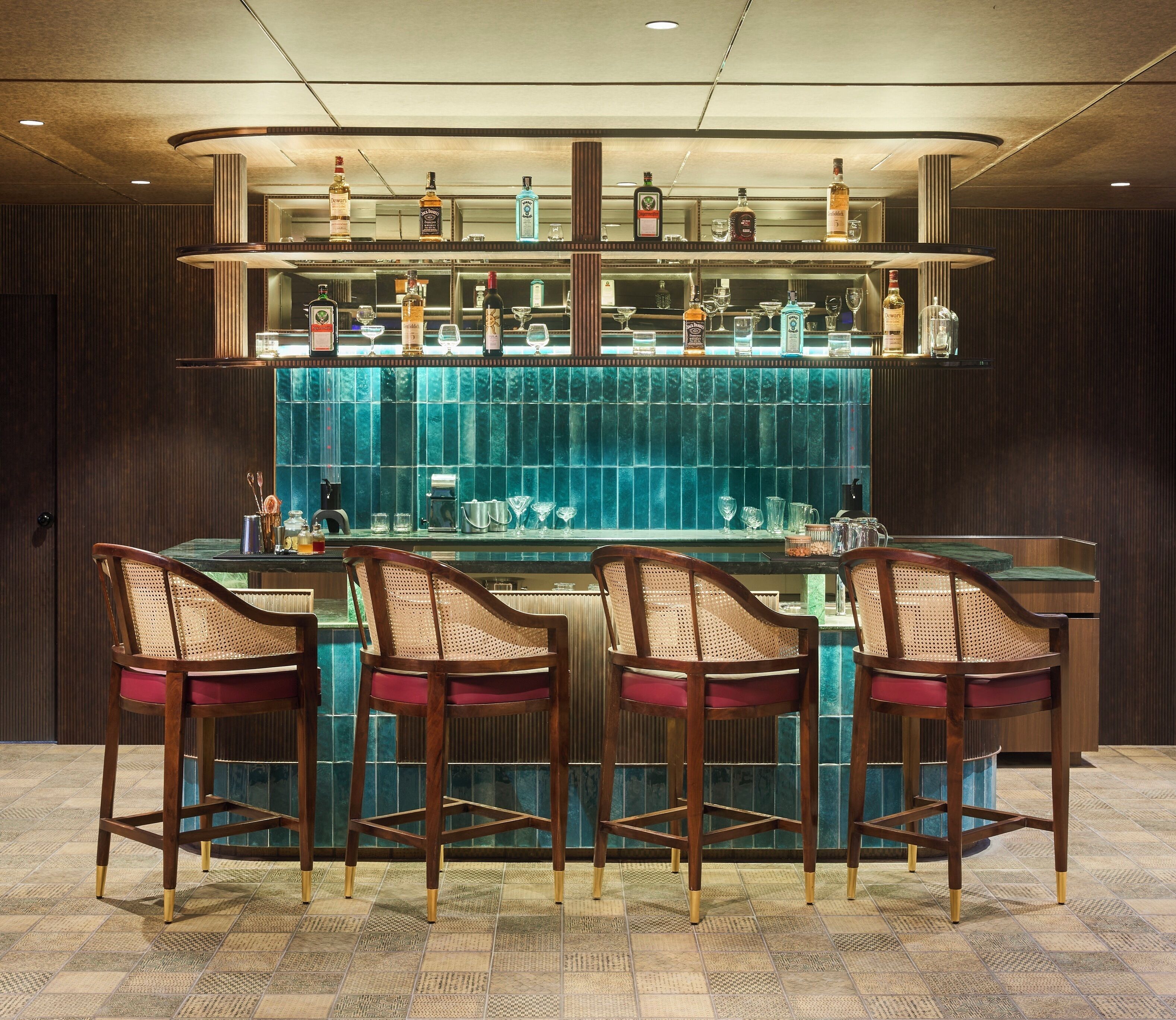 A bar area with a glass counter, multiple liquor bottles, and four wooden chairs with cushioned seats.