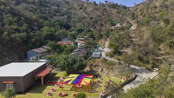 A hillside view of a building with a red roof, a colorful outdoor seating area, and a paved path.