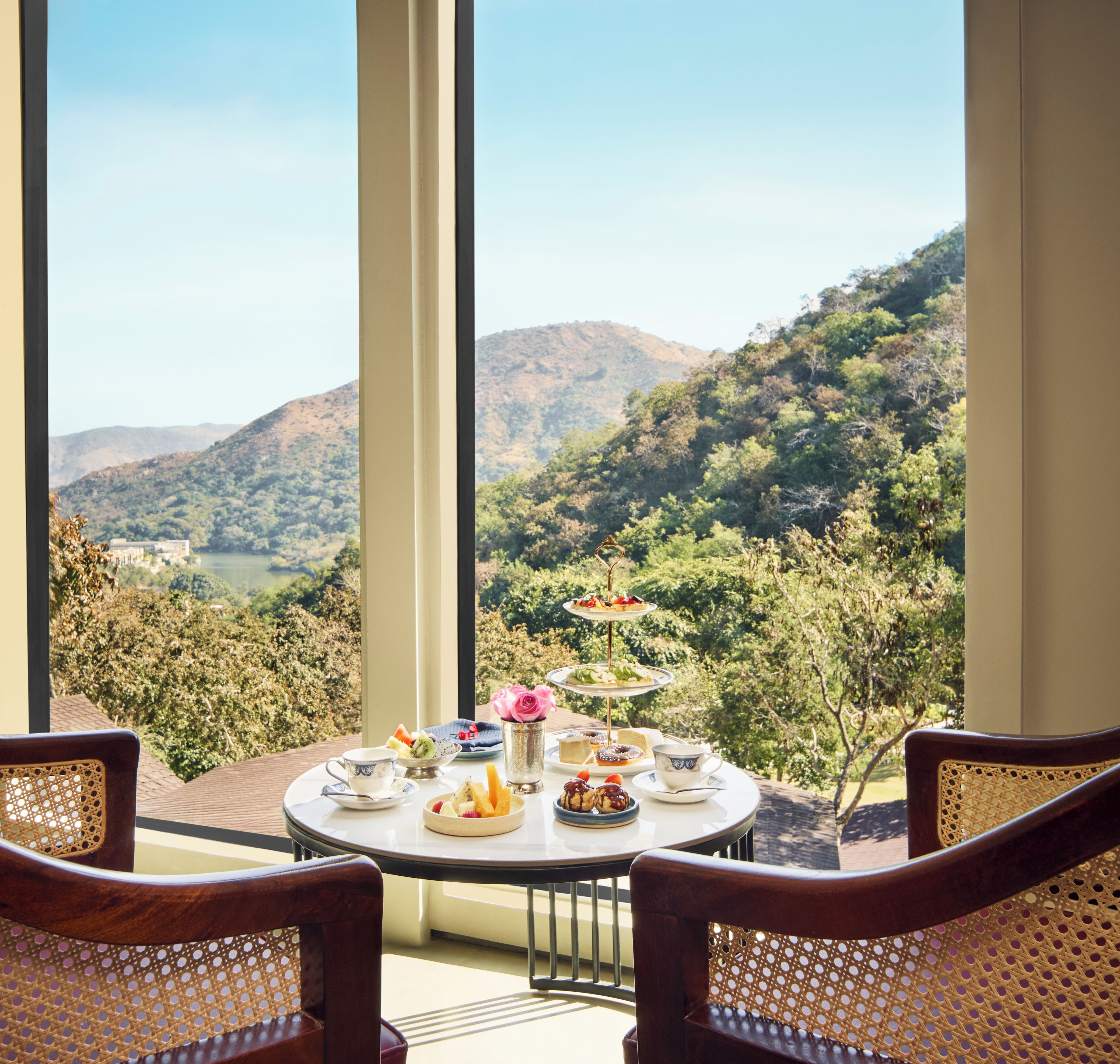 Una mesa de comedor con vistas panorámicas, dos sillas y un expositor de postres con pasteles.