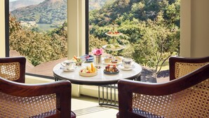 A table with a view of a mountainous landscape, two chairs, and a dessert tray. - Treat Aranya Resort (Kumbhalgarh)