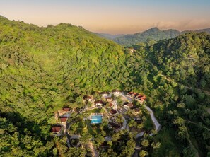 Vista aérea de un complejo turístico con varias edificaciones, una piscina y un camino sinuoso a través de una zona boscosa.