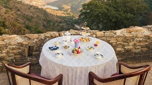 A round table with a floral tablecloth set for a meal, overlooking a mountainous landscape. - Treat Aranya Resort (Kumbhalgarh)