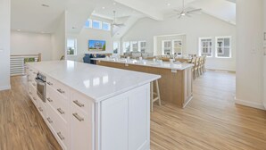 Une cuisine spacieuse dotée d’un grand îlot central, de meubles en bois et d’un plafond haut avec des fenêtres de toit.