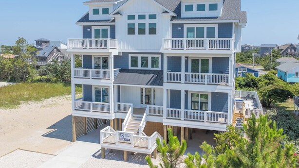 Une propriété en bord de mer, composée de plusieurs étages, dotée de balcons, d’une terrasse couverte et d’une plage de sable.