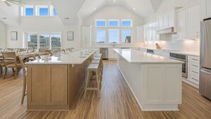 Une cuisine spacieuse dotée d’un grand îlot central, de planchers en bois et de meubles de cuisine blancs.