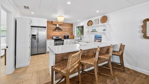 Une cuisine moderne avec des meubles blancs, un grand îlot central doté de tabourets et un mur d’accent en bois.