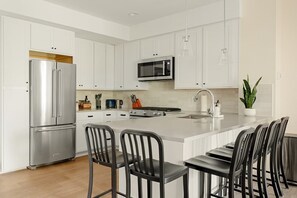A modern kitchen with white cabinetry, stainless steel appliances, and a central island with bar stools. - Heart of Olde Town | Urban Retreat | 95 Walk Score (Arvada)