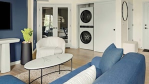 Un salon moderne avec un canapé, une table basse et un téléviseur. Il y a également un espace buanderie équipé de deux machines à laver.