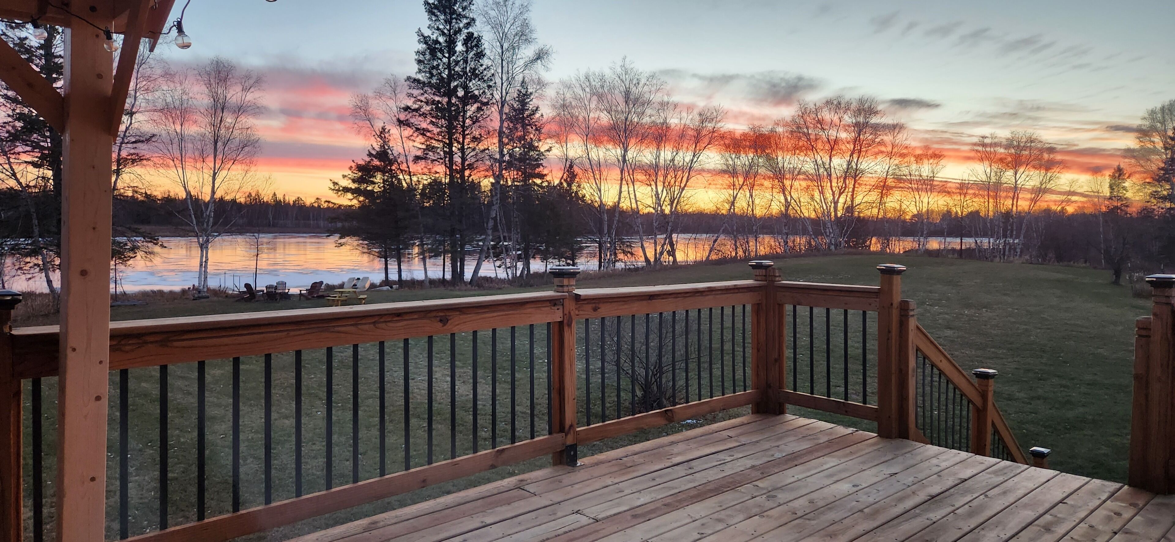 Une terrasse en bois avec une rambarde, donnant sur un lac au coucher du soleil.