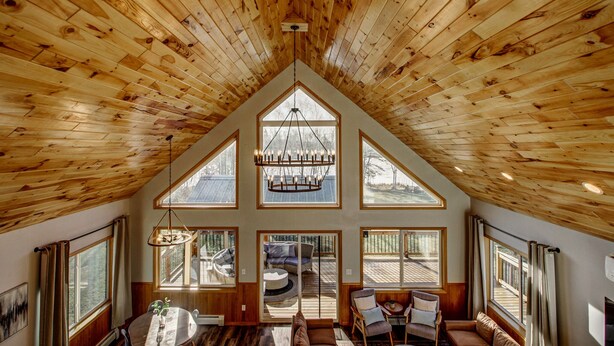 A spacious loft with a high ceiling and large windows, featuring a dining area and seating by a deck.