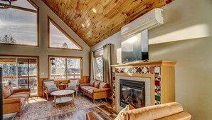 A spacious living room with a fireplace, large windows, and a wooden ceiling.