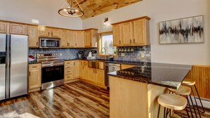 A modern kitchen with wooden cabinets, stainless steel appliances, a black countertop island, and a hanging light fixture.