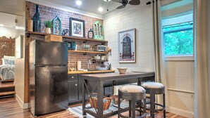 Una cocina con refrigerador, estantes de madera, una ventana y un ventilador de techo.