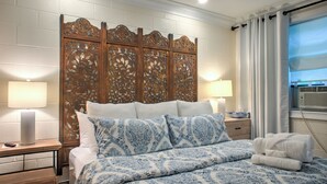 Un dormitorio con una cama grande, cabecera de madera, dos mesitas de noche con lámparas, una ventana con cortinas y vistas al exterior.