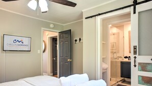 A hotel room with a bed, a TV displaying the hotel name, a door to the bathroom, and a shower area.