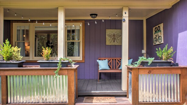 A porch with a wooden bench, potted plants, and a welcome mat.