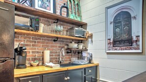 A kitchen with a brick wall, wooden shelves, a sink, and a coffee maker.