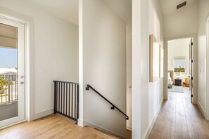 Un pasillo limpio y moderno con suelo de madera, barandilla negra y una puerta que da a un espacio exterior.
