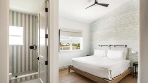 Un dormitorio con cama de madera, ventana con persianas, ventilador de techo y pared con diseño de ladrillo.
