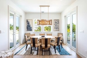 A dining room with a round table, six chairs, a hanging light fixture, and artwork on the walls. - Altair House at Lunara Bay (Key West)