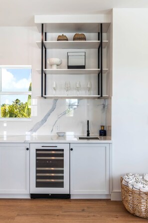 Eine moderne Küche mit weißen Schränken, einer Marmor-Spritzschutzwand und einem integrierten Weinkühlschrank.