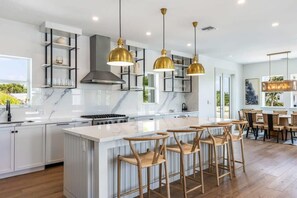 A modern kitchen with white cabinetry, a marble countertop, and a central island with bar stools. - Altair House at Lunara Bay (Key West)
