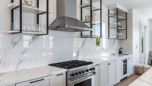 A modern kitchen with a gas stove, oven, and built-in shelves. - Altair House at Lunara Bay (Key West)