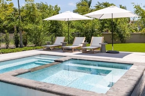 A rectangular swimming pool with a stone border, surrounded by lounge chairs and umbrellas.