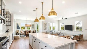 Una cocina moderna con una isla grande, iluminación colgante y un comedor con sillas y una mesa.